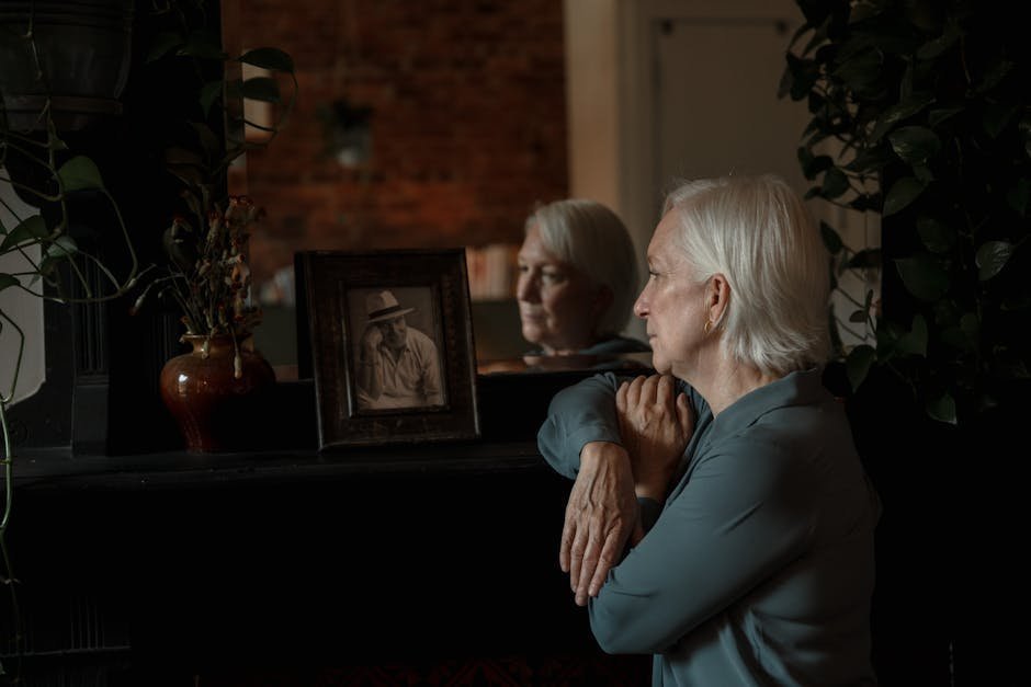 Older woman sitting alone with a framed photograph of her dog and a sympathy card on the table